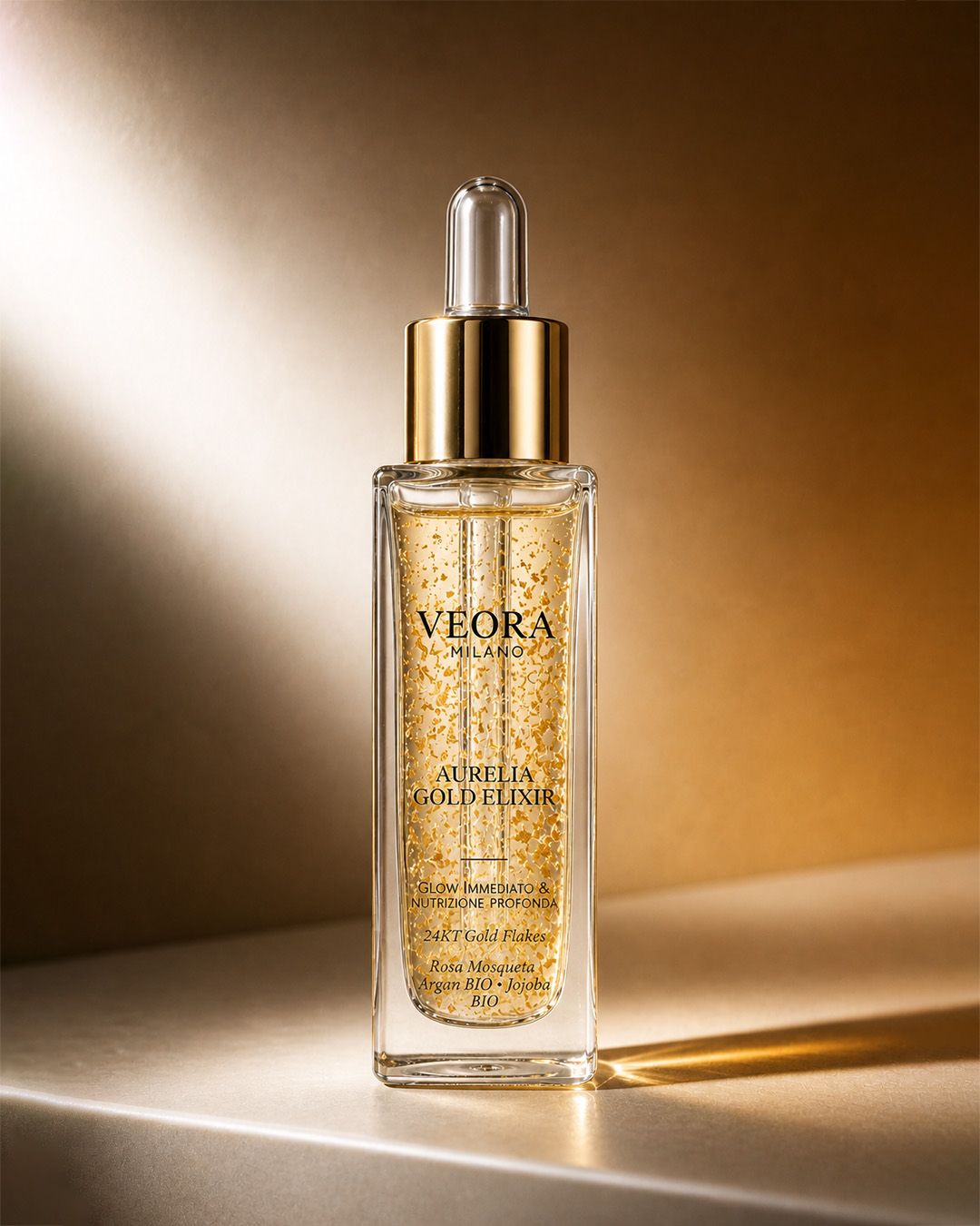 Flacone contagocce di Veora Milano Aurelia Gold Elixir su una superficie riflettente con uno sfondo caldo.