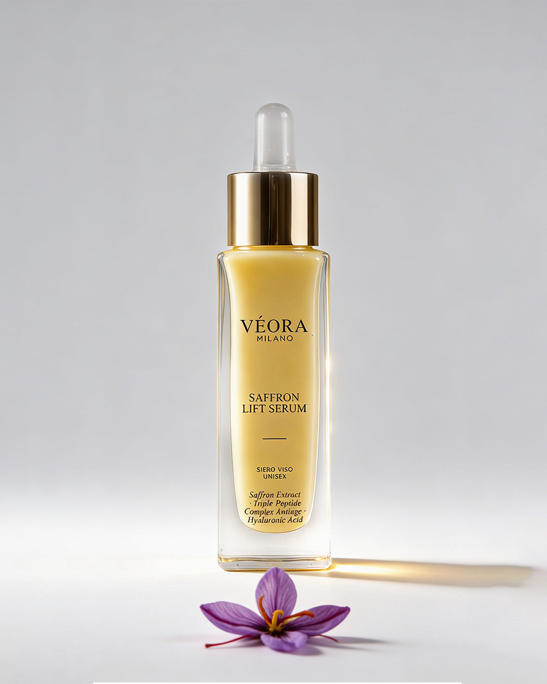 Flacone del siero lifting allo zafferano Véora Milano con fiore di zafferano viola su sfondo grigio chiaro.