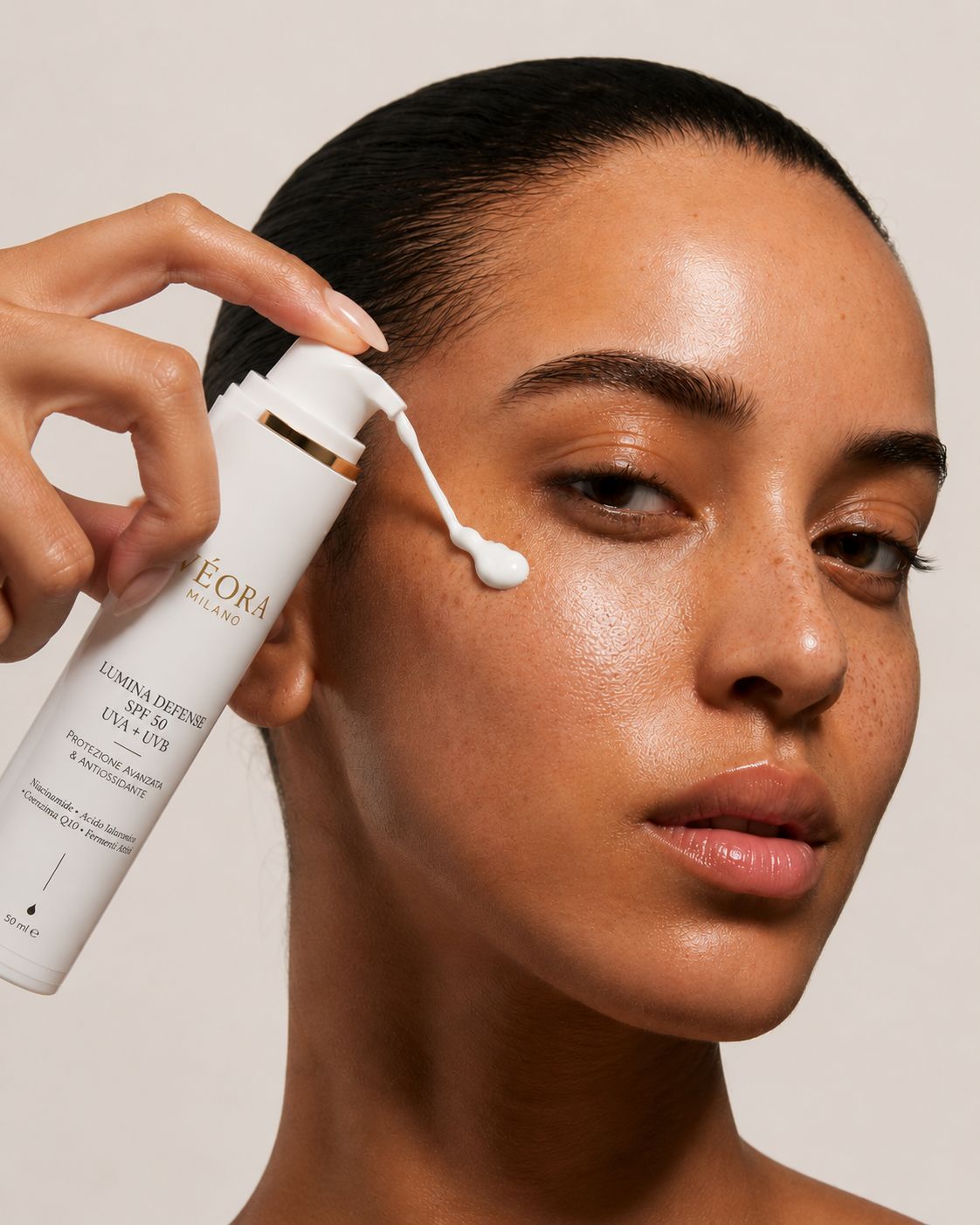 Una donna applica sul viso la crema solare Lumina Defence SPF 50, su uno sfondo beige.