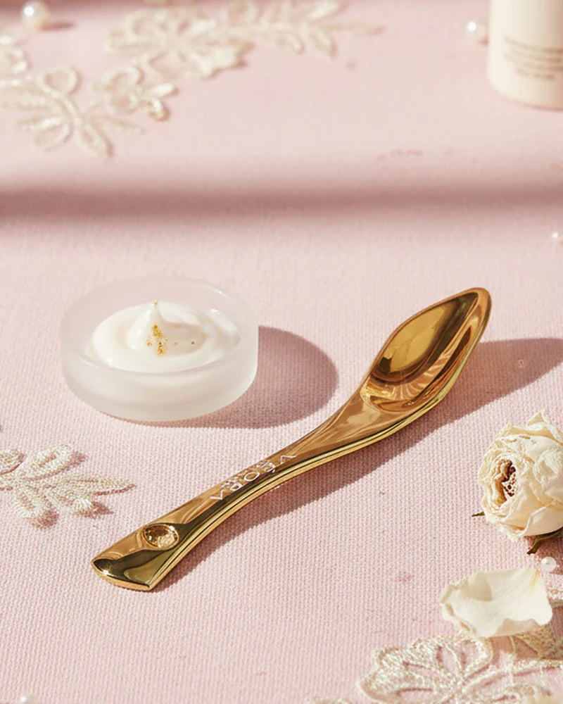 Veora Milano Cucchiaio dorato su superficie rosa con elementi decorativi